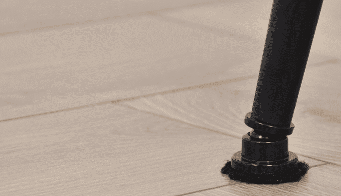 Close-up van een ronde stalen stoelpoot met scratchnomore footfixx hollow stoeldop op houten vloer